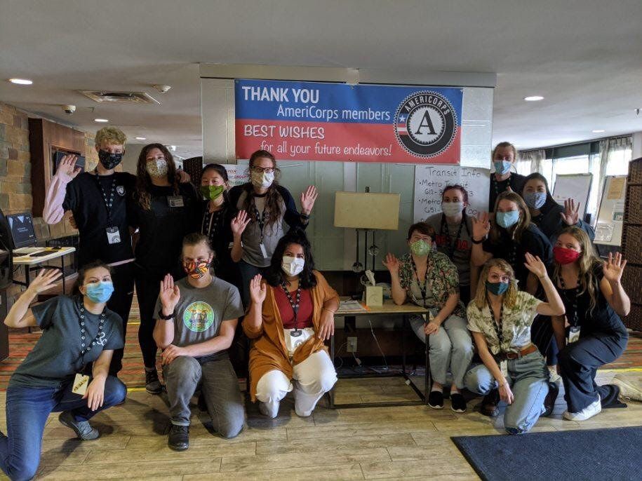 A group of people standing and kneeling around a sign thanking AmeriCorps members