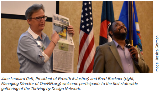 Jane and Brett stand side by side. Jane holds a newspaper; Brett holds a microphone