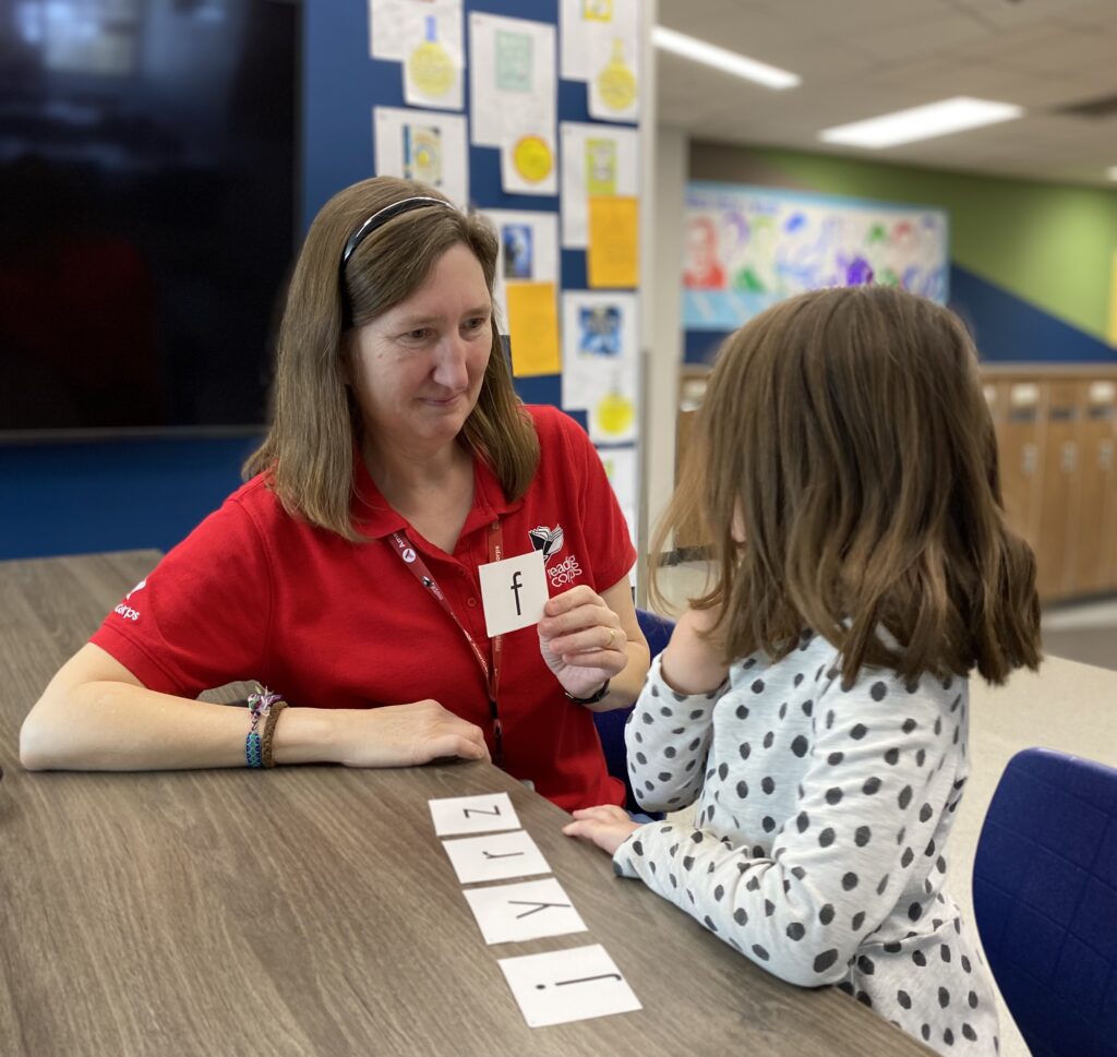 An adult in a red shirt holds up a letter card in front of a child.